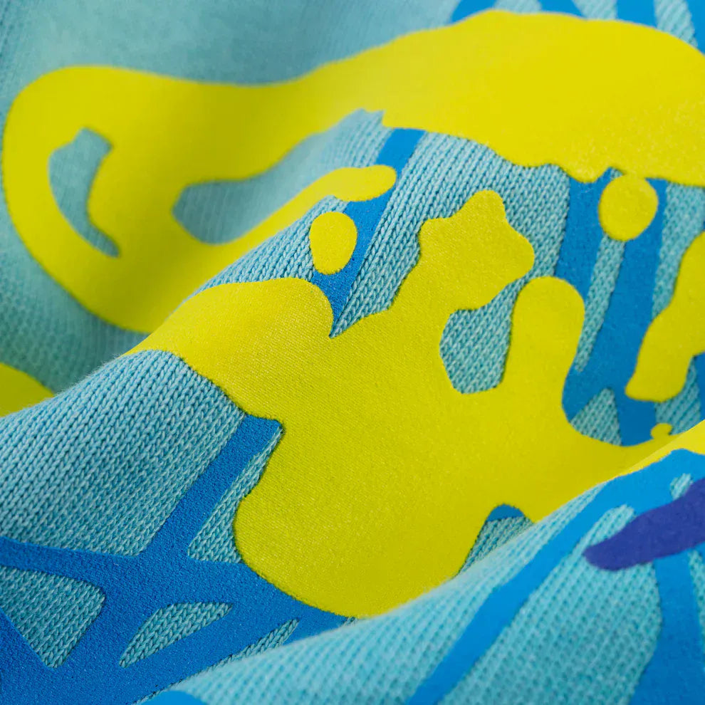 Close-up of 100% Cotton Sp5der Sweatpants in blue, showing spider web graphic and star details. The fabric’s texture and print quality are clear, making these relaxed fit joggers perfect for unisex streetwear.