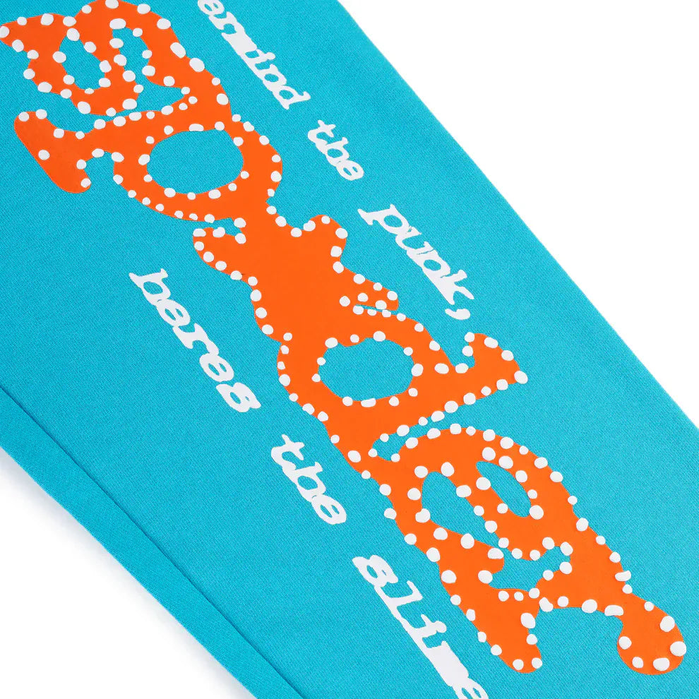 Close-up of 100% Cotton Sp5der Sweatpants—Unisex teal jogger pants with a relaxed fit, featuring bold orange logo print and white "behind the punk, bares the alien" text. Unique, comfortable streetwear style.
