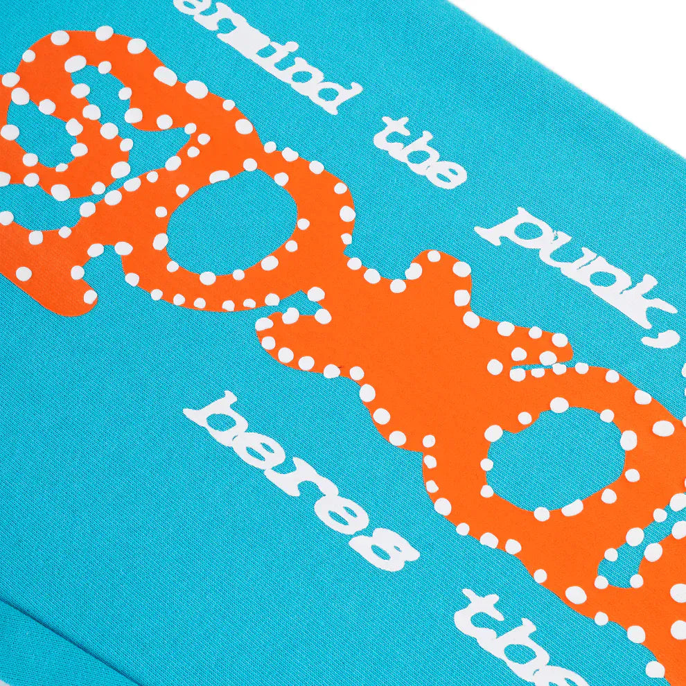 Close-up of unisex Sp5der sweatpants made from 100% cotton in teal, showcasing a large orange logo print and playful white text for a relaxed streetwear look.