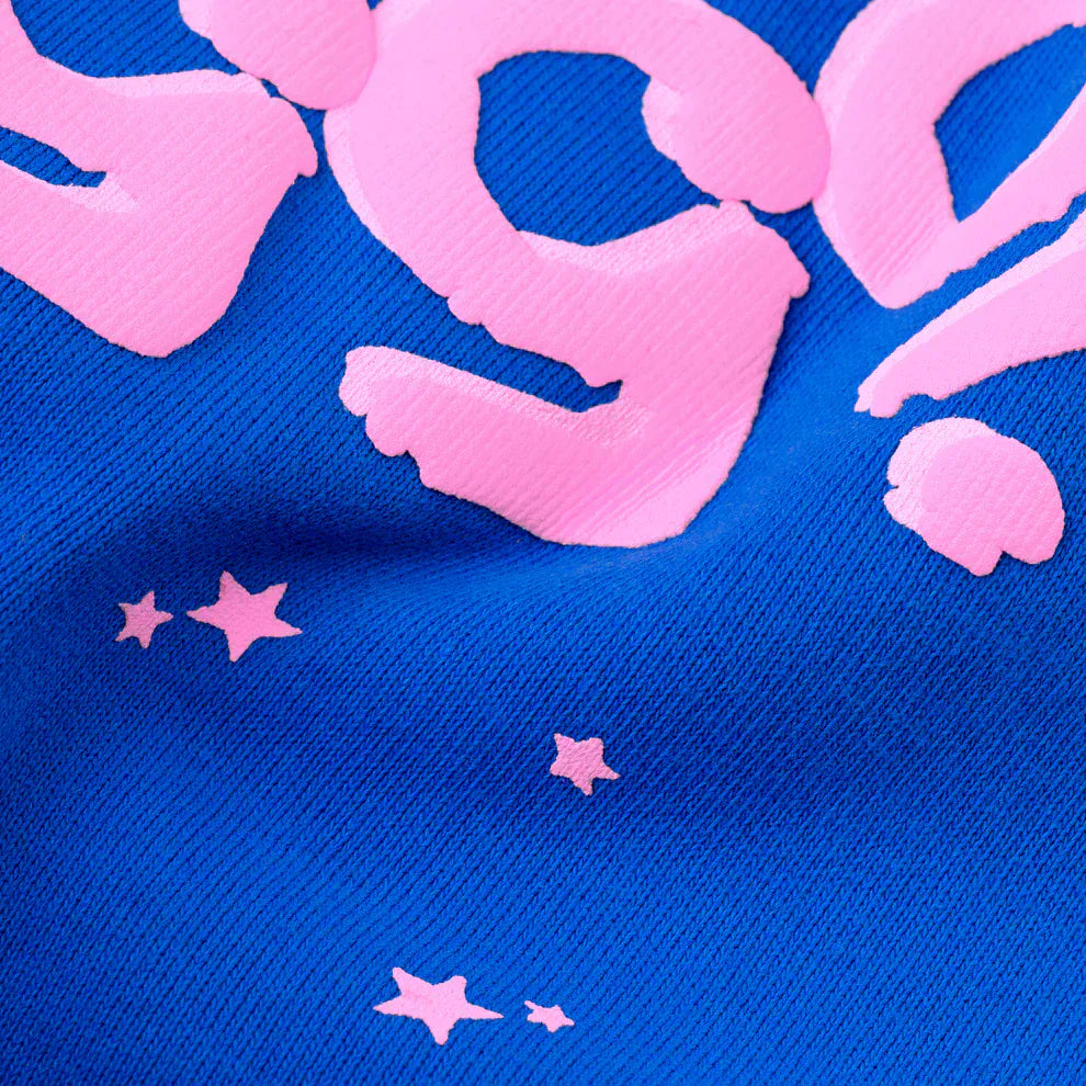 Close-up of 100% Cotton Sp5der Sweatpants—Unisex Blue Jogger Pants featuring a raised pink logo and star accents, highlighting their relaxed fit and trendy streetwear style.