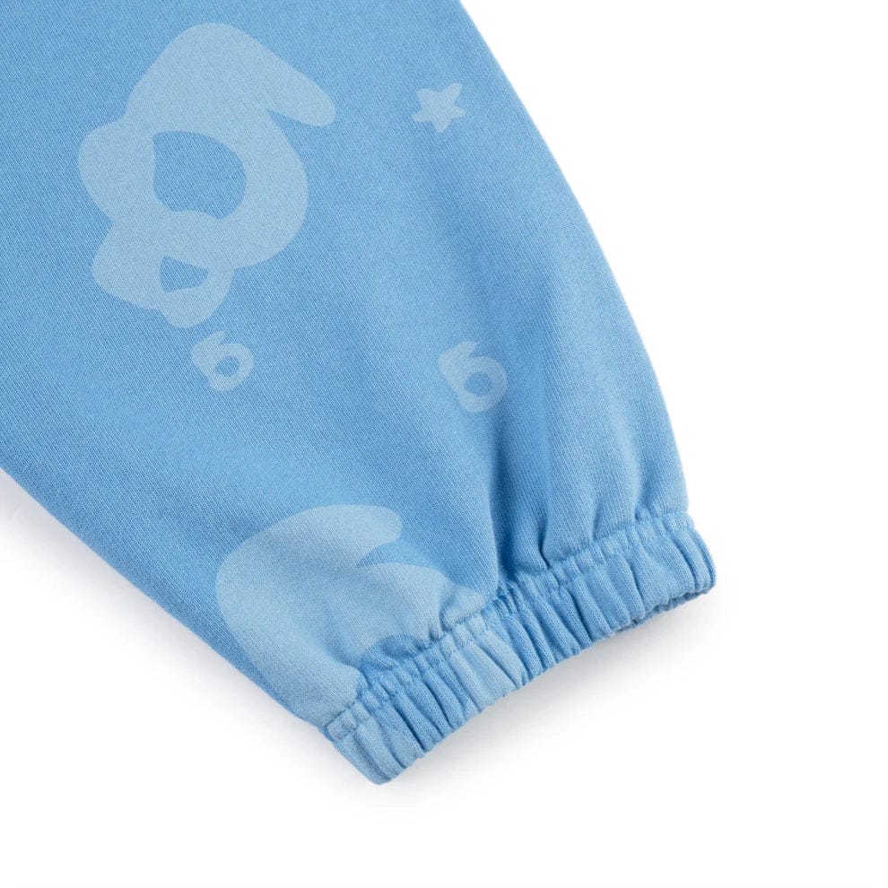 A close-up of Sp5der Light Blue All-Over Print Sweatpants, made from 100% cotton with elastic cuffs, featuring abstract shapes, stars, and the number 6—unisex streetwear joggers.