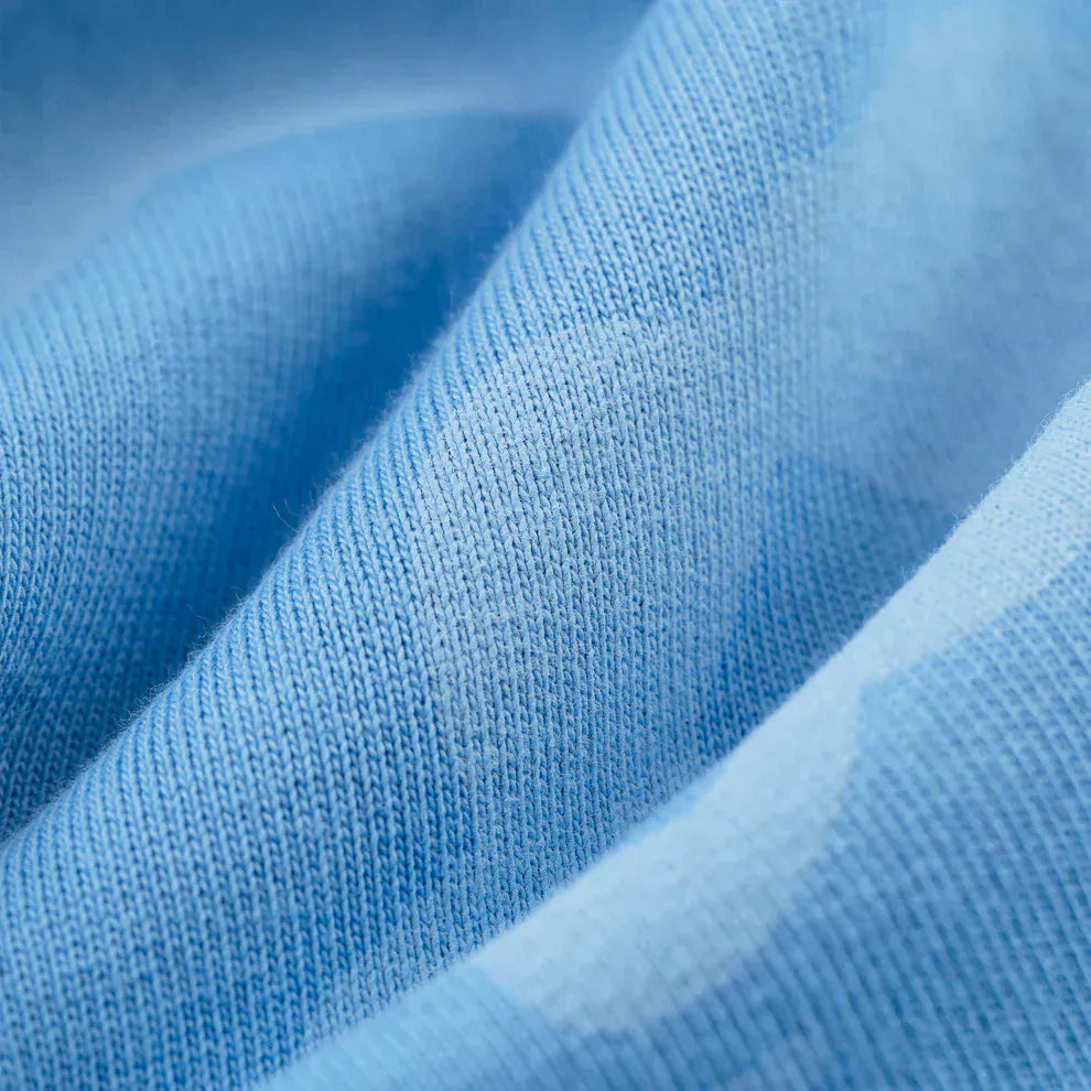 Close-up of the Sp5der Light Blue All-Over Print Sweatpants shows visible knit texture and soft folds, highlighting the premium 100% cotton quality of these unisex streetwear joggers.