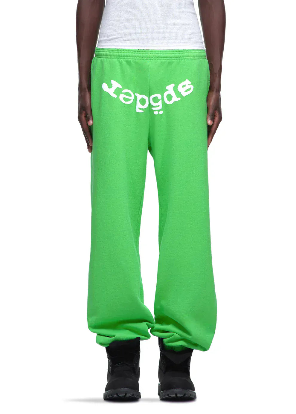 A person wearing Sp5der Sweatpants – Unisex Green Cotton Sweatpants with a front logo print, styled with black shoes and a white tank top, showcasing bold streetwear fashion.