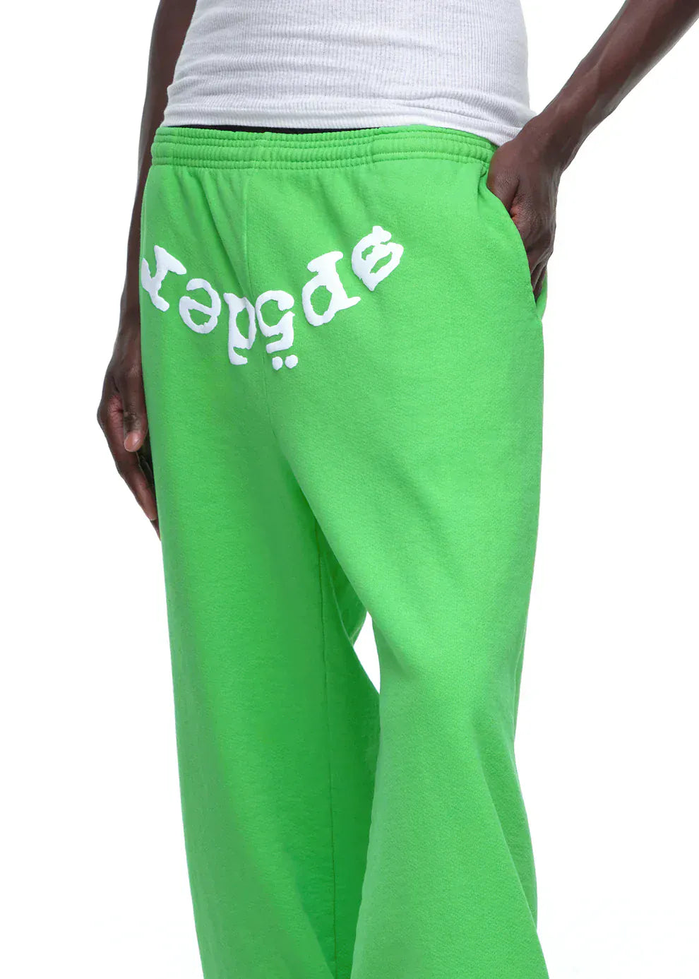 Someone wears Sp5der Sweatpants – Unisex Green Cotton Sweatpants with a front logo print, paired with a white ribbed tank top for a bold, streetwear-inspired look.