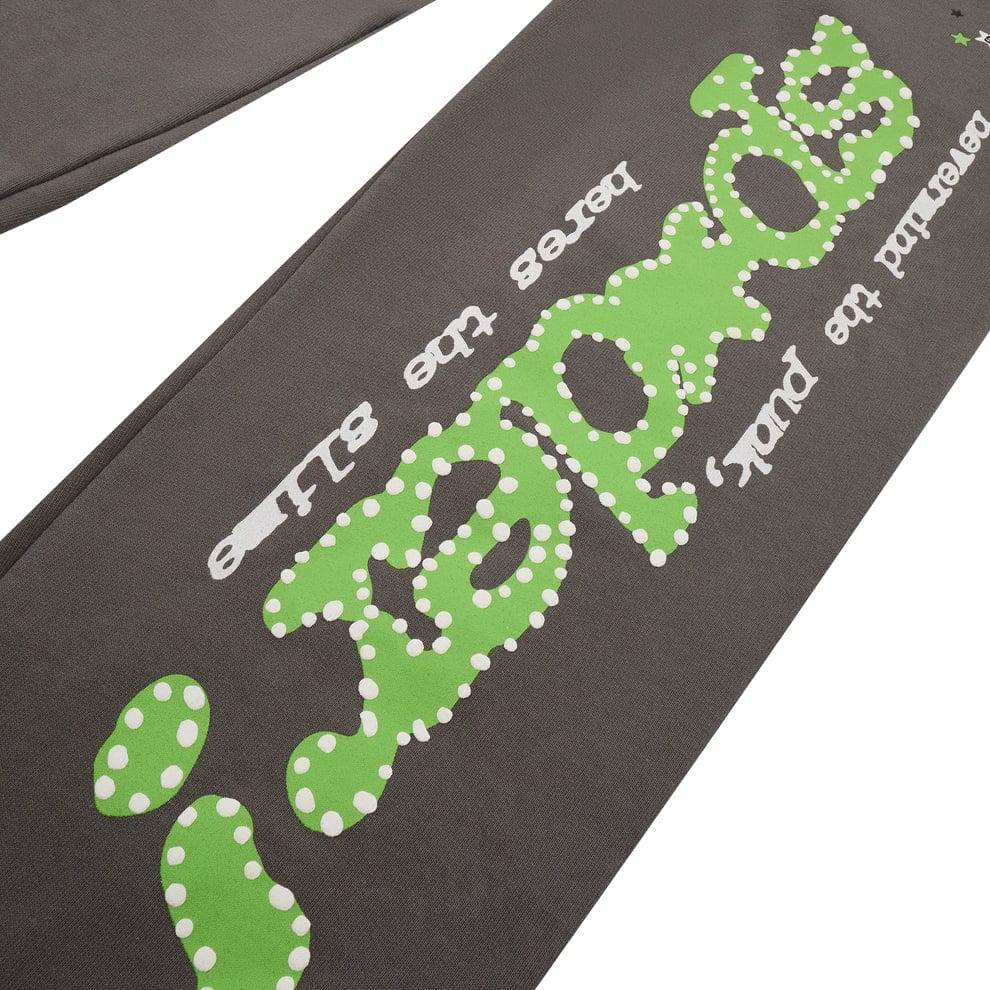 Close-up of Sp5der Sweatpants – Unisex Dark Grey Cotton Sweatpants featuring a green side logo, star print, and streetwear-inspired text "leaps the slide" and "behind the pull" in green and white.