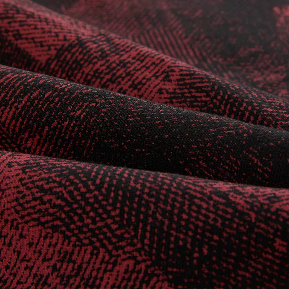 Close-up of Sp5der Sweatpants—unisex red and black patterned cotton sweatpants with graphic detail. The geometric, pixelated fabric design and folded surface make them ideal for stylish streetwear joggers.