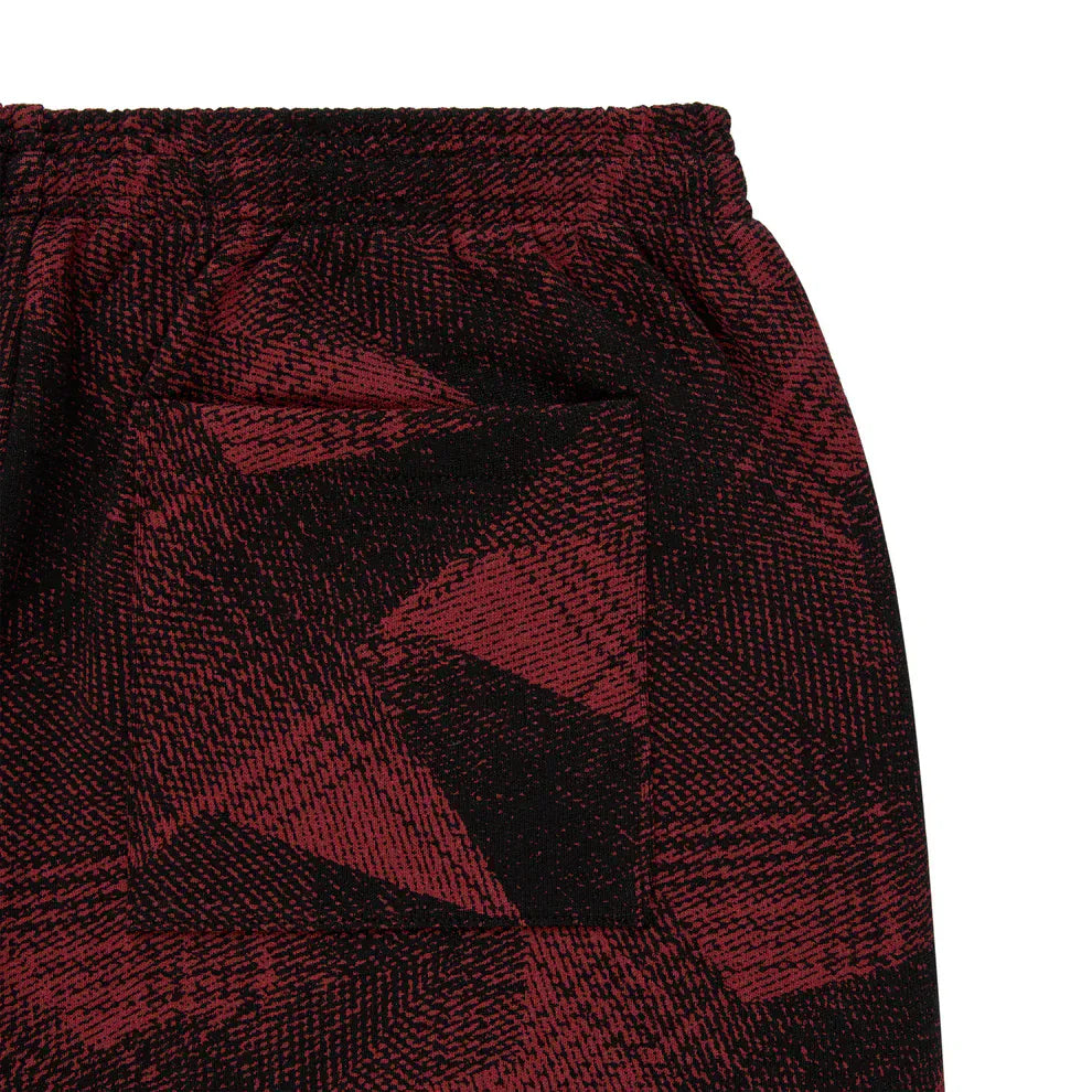 Close-up of Sp5der Sweatpants—unisex red and black patterned cotton joggers with graphic detail, a visible pocket, and elastic waistband, offering a stylish streetwear look.