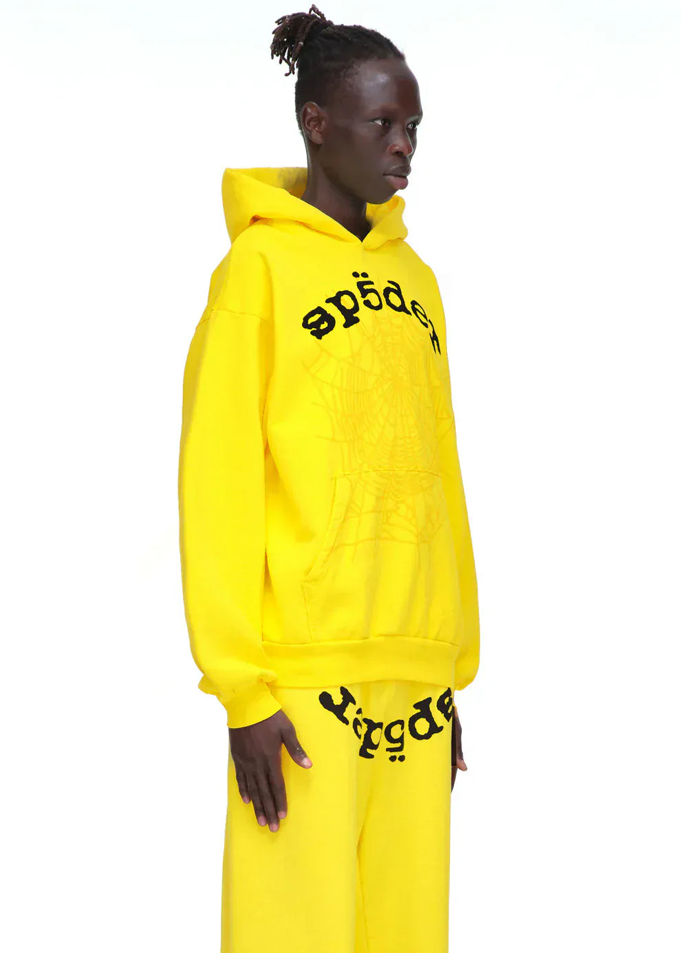 Model wears a Yellow Graphic Hoodie with Spider Web Print and Lettering – Comfort Fit Pullover Hoodie with matching pants, standing against a white background for standout streetwear style.