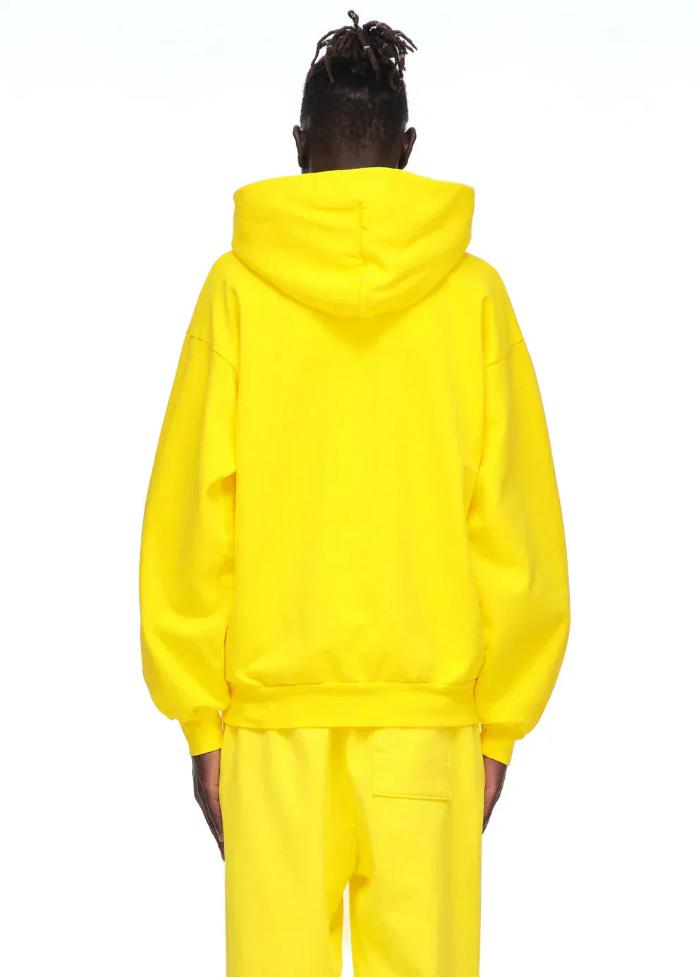 A person faces away from the camera in a Yellow Graphic Hoodie with Spider Web Print and Lettering – Comfort Fit Pullover Hoodie and matching pants, creating a bold streetwear look against a plain white background.