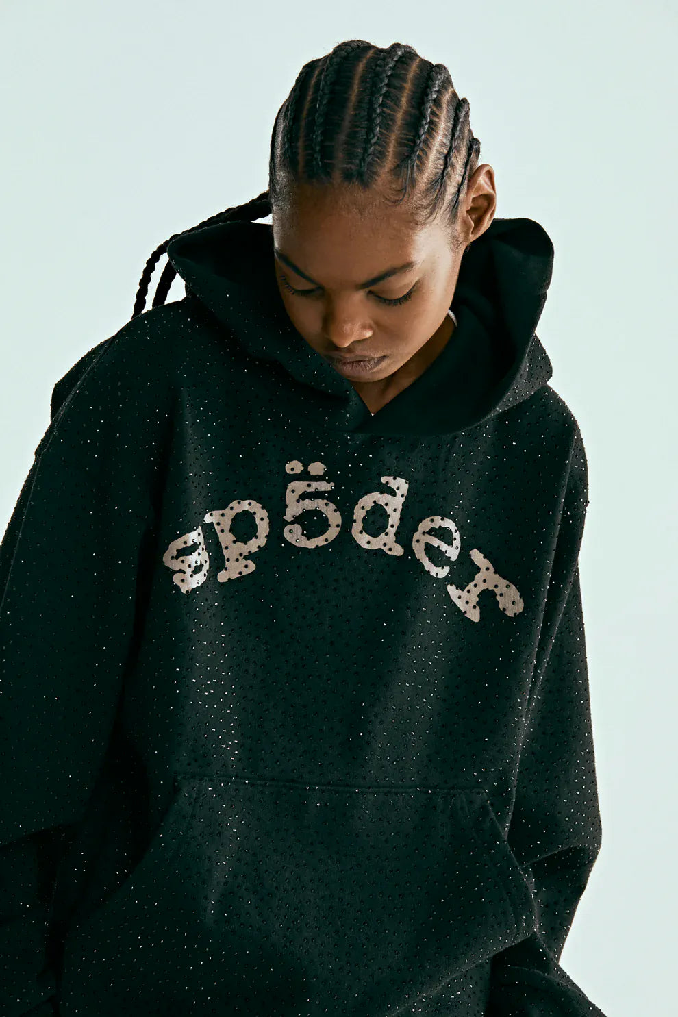 A person with braided hair looks down while wearing the VVS Spider Hoodie – a black Sp5der rhinestone pullover featuring diamond graphic detail.