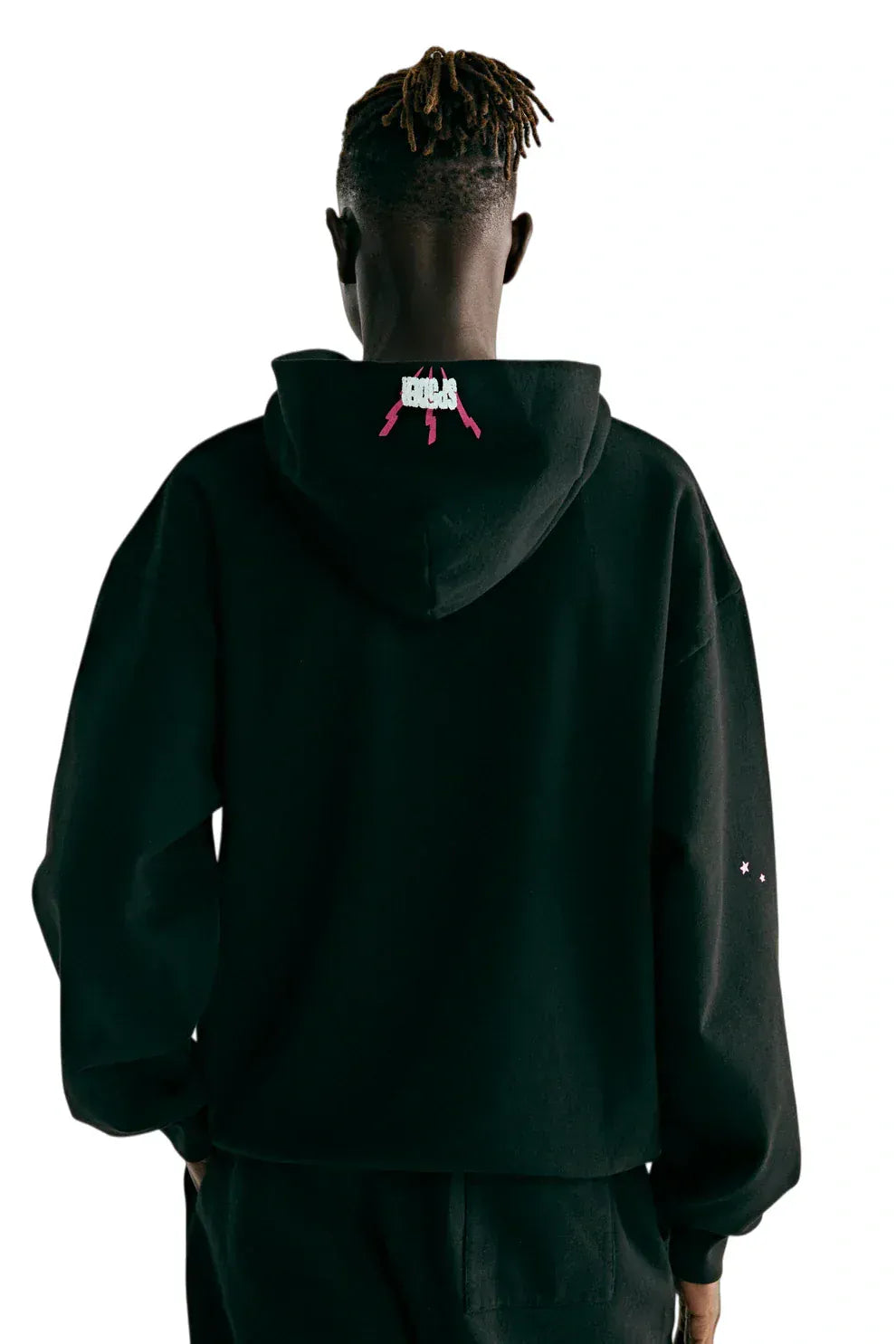 Person stands with back to camera, wearing the Sp5der 555 Hoodie – Black & Pink Web 440GSM Heavyweight Streetwear Pullover, featuring a small graphic of two pink guns and white text on the hood—ideal for Y2K-inspired luxury street style.
