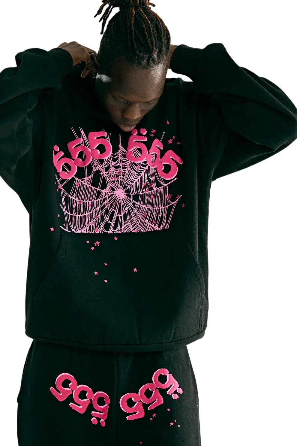 Wearing the Sp5der 555 Hoodie – Black & Pink Web 440GSM Heavyweight Streetwear Pullover, styled with matching pants featuring bold "555" and "999" pink graphics and a spiderweb design, channeling Y2K street fashion while adjusting the hood.