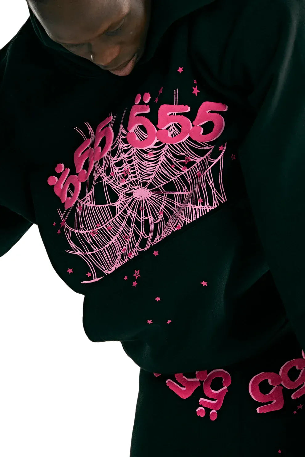 Wearing the Sp5der 555 Hoodie – Black & Pink Web 440GSM Heavyweight Streetwear Pullover with bold pink Arabic lettering and graphic, paired with black pants with pink text, channels Y2K style on a clean white backdrop.